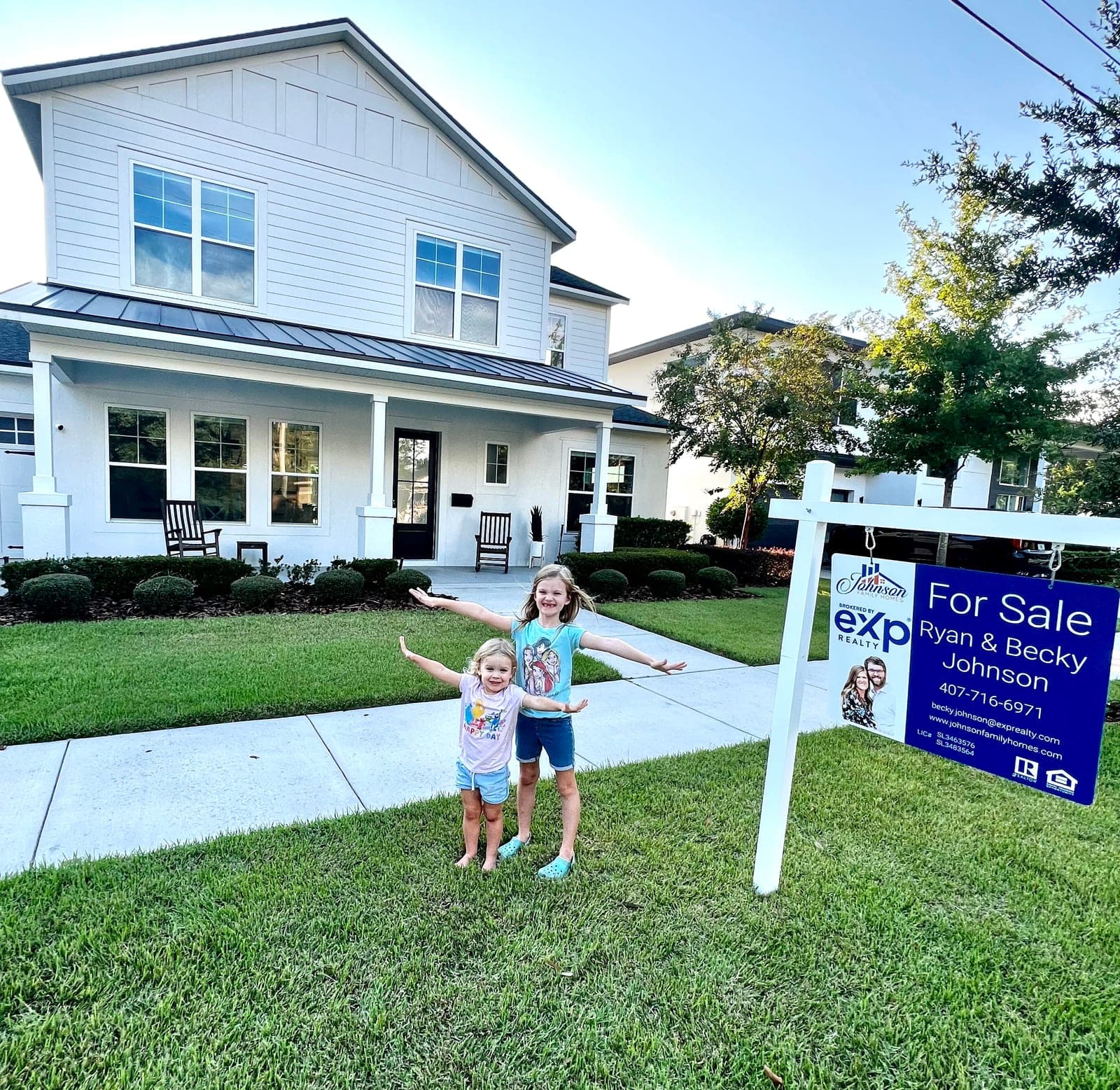 Two of the Johnson kids on the front lawn of a Johnson Family Homes listing, with a For Sale sign showing Ryan & Becky Johnson