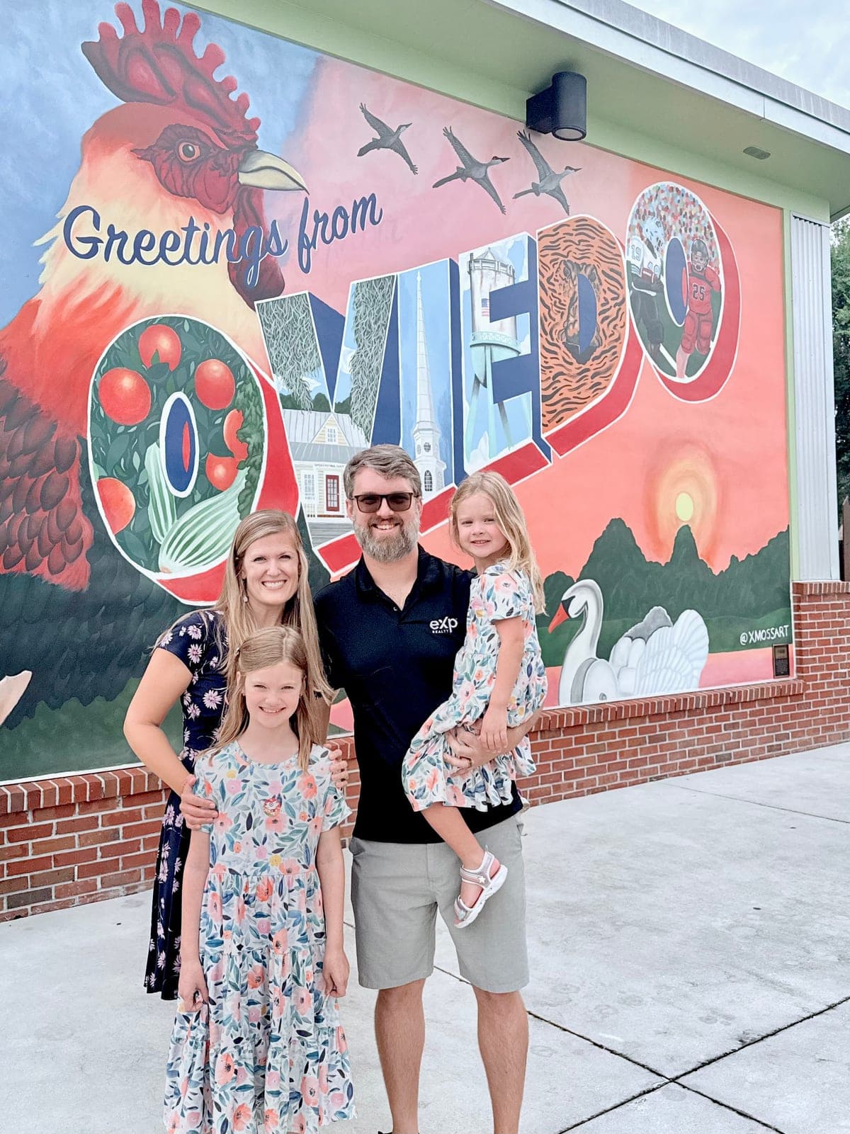 Becky and Ryan Johnson with their two daughters in front of the 'Greetings from Oviedo' mural